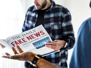 Mies lukee lehteä, jonka kannessa lukee "Fake news"