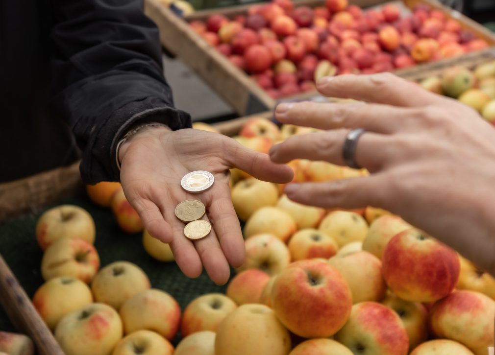 Personen räcker en annan mynt över affärens äppelverk.