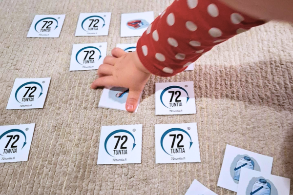 Muistipelikortteja, joissa 72 tuntia -logo) jaettuna alustalle kuvapuoli alaspäin. Pieni lapsen käsi tarttumassa yhteen korteista. Vieressä kuvapuoli ylöspäin saatu pari, jossa vesitonkan kuva.
