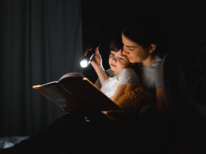 Äiti ja lapsi lukevat kirjaa sylikkäin taskulampun valossa